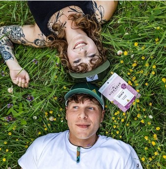 Two people laying on grass with High Road Edibles gummies package between them